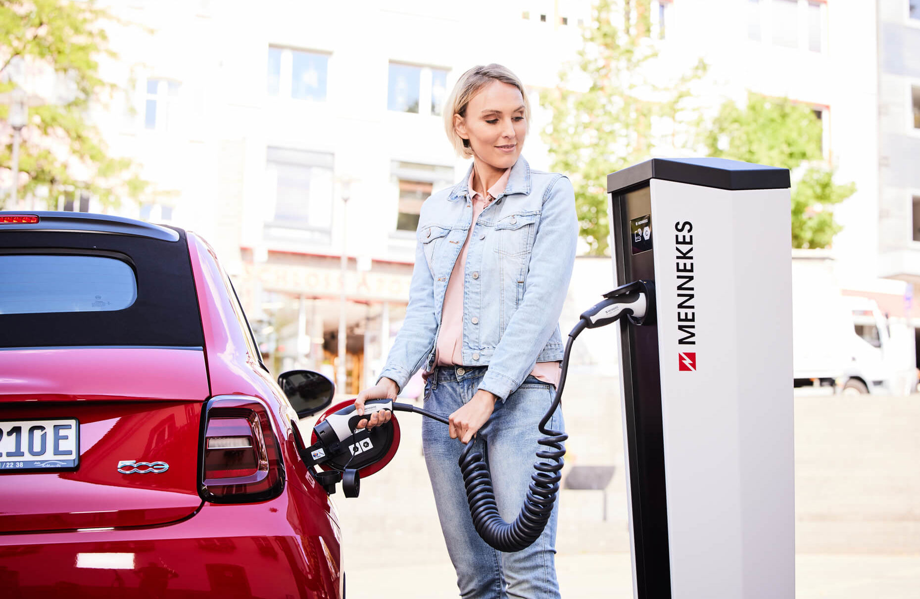 Eine Frau nutzt ein spiralisierte Typ2 Ladekabel um Ihr Elektroauto an einer öffentlichen Ladesäule anzuschließen